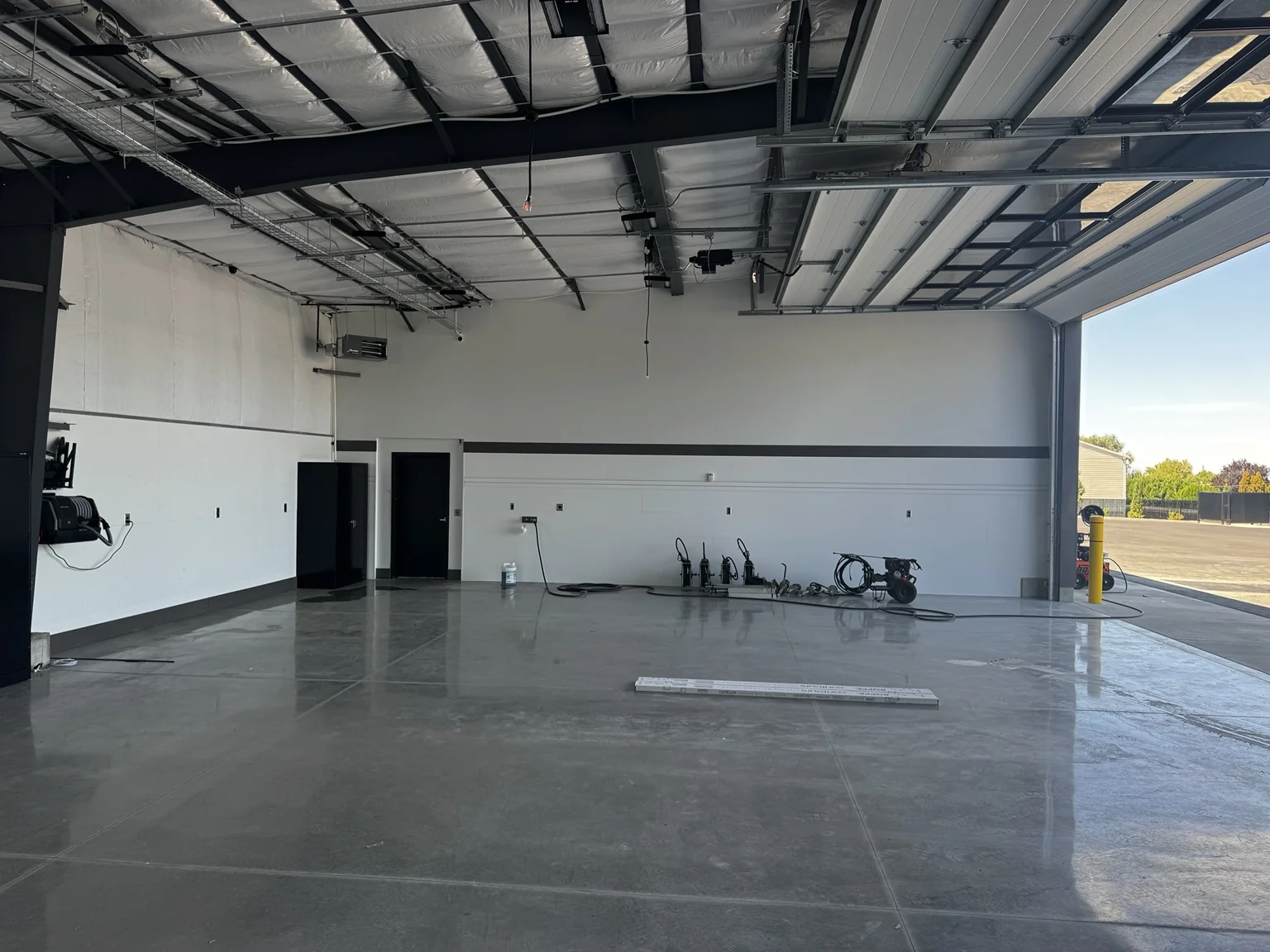 Open boat-shop work bay with polished concrete, white walls, black trim, and a raised overhead door