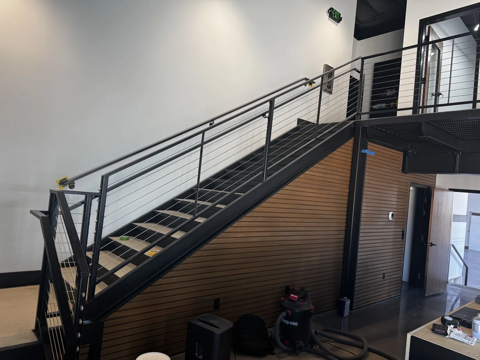 Black steel boat-shop staircase with cable railings beside a warm wood-slat accent wall
